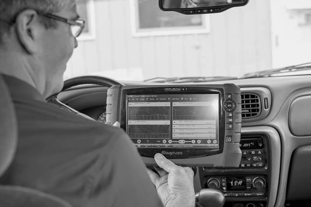 A mechanic in the driver's seat uses a diagnostic tablet inside a vehicle.