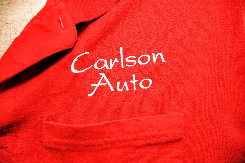 Close detail of the real Carlson Auto name embroidered above a work-shirt pocket.