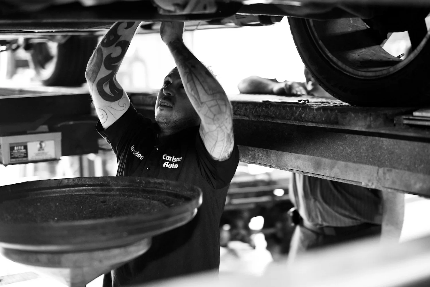 A Carlson Auto mechanic reaches up to work underneath a vehicle on a lift.
